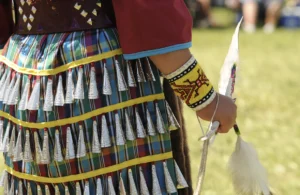 person faces away from the camera wearing a jingle dress and other indigenous clothing