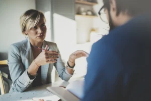 woman sits across a desk from a man and explains something