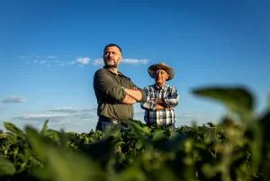 two farmers with their arms crossed look over a field of soybeans