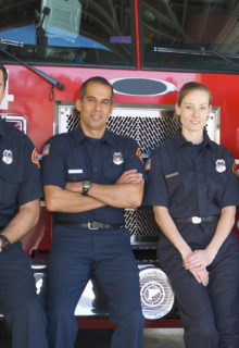 Firefighters leaning against a red fire truck