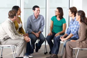 smiling adults sit in a circle of chairs