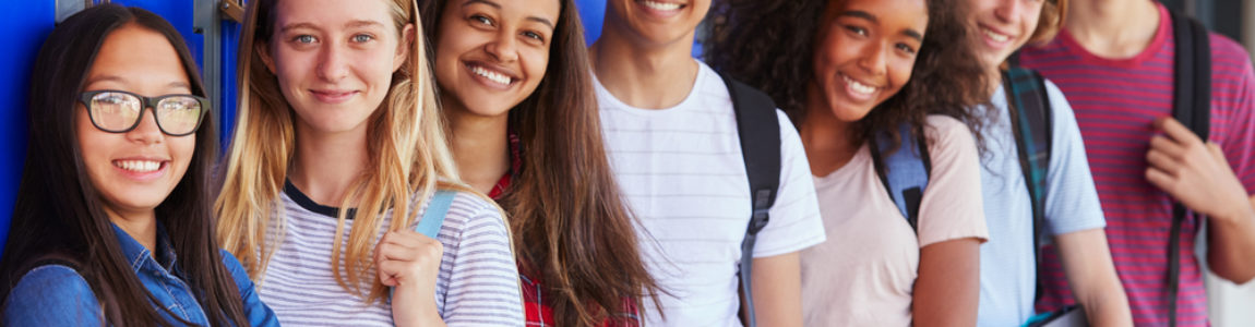 smiling teens lined up in front of a wall of blue lockers