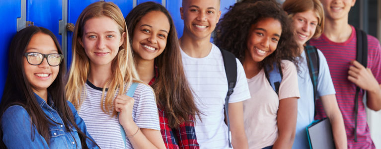 smiling teens lined up in front of a wall of blue lockers