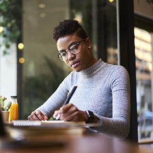 young person sits writing at a cafe table