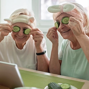 two smiling old women in spa clothes put cucumber slices on their eyes