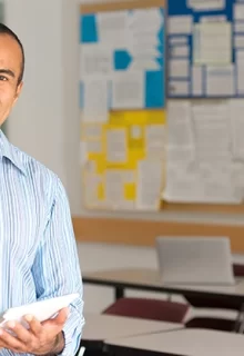 smiling male teacher stands in a classroom