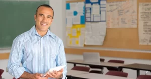 smiling male teacher stands in a classroom