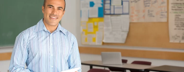 smiling male teacher stands in a classroom