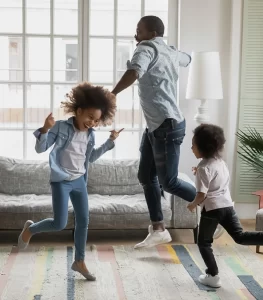 dad and two young kids dance around the living room