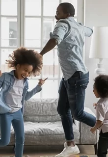 dad and two young kids dance around the living room