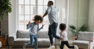 dad and two young kids dance around the living room