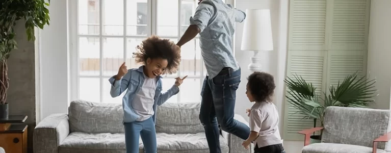 dad and two young kids dance around the living room