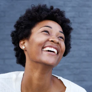 young black woman stands in front of a blue wall smiling joyfully