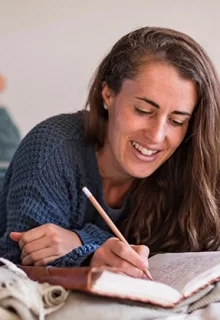 smiling woman lying on bed and writing in journal