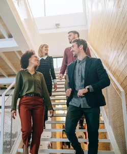 four smiling colleagues walk down a sunlit staircase together