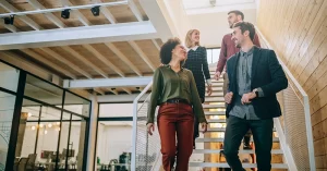 four smiling colleagues walk down a sunlit staircase together