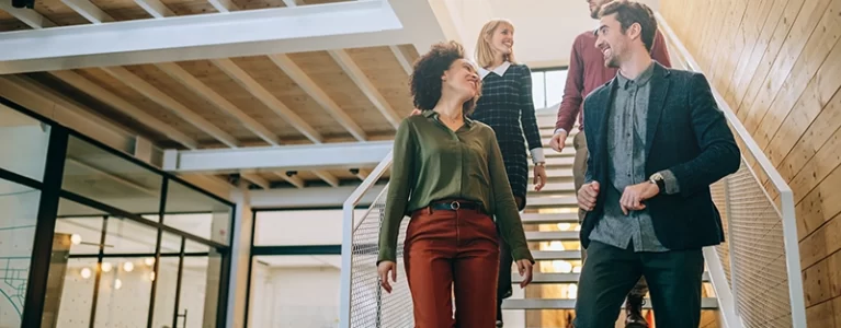 four smiling colleagues walk down a sunlit staircase together