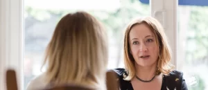 two women talk across a kitchen table