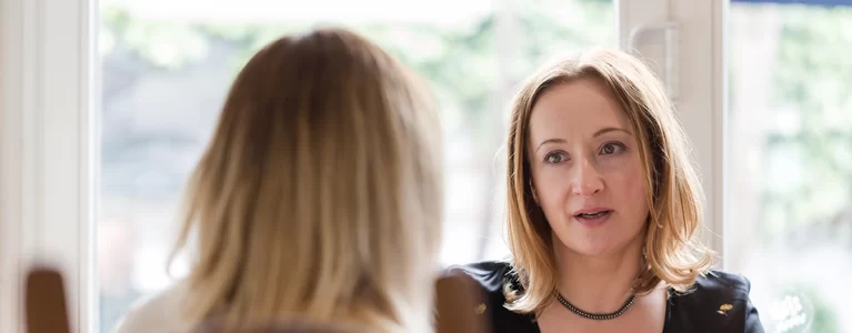 two women talk across a kitchen table