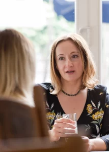two women talk across a kitchen table