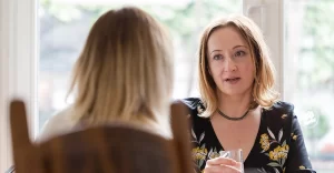 two women talk across a kitchen table