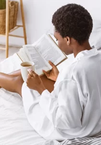 Black woman reads in bed with a cup of coffee
