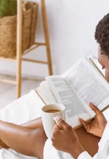 Black woman reads in bed with a cup of coffee