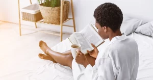 Black woman reads in bed with a cup of coffee