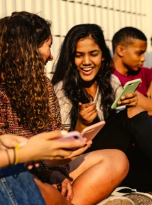 group of smiling teens showing each other stuff on their cell phones