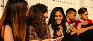 group of smiling teens showing each other stuff on their cell phones