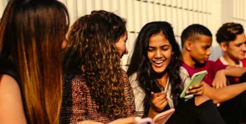 group of smiling teens showing each other stuff on their cell phones