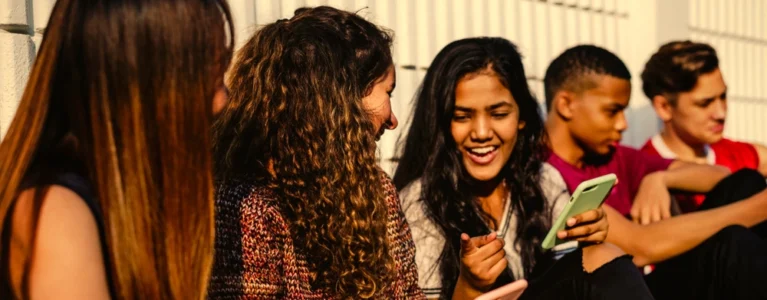 group of smiling teens showing each other stuff on their cell phones