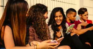 group of smiling teens showing each other stuff on their cell phones