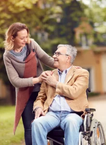daughter standing and father in a wheelchair smile at each other