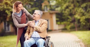 daughter standing and father in a wheelchair smile at each other
