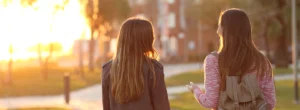 two young women walk outside on a path and talk