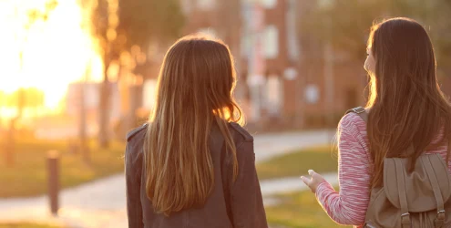 two young women walk outside on a path and talk