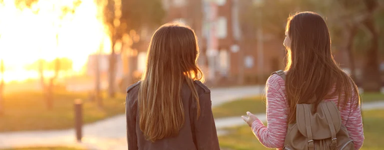 two young women walk outside on a path and talk