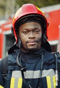young black male firefighter stands in front of a firetruck