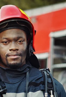 young black male firefighter stands in front of a firetruck