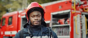 young black male firefighter stands in front of a firetruck