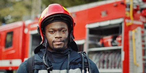 young black male firefighter stands in front of a firetruck