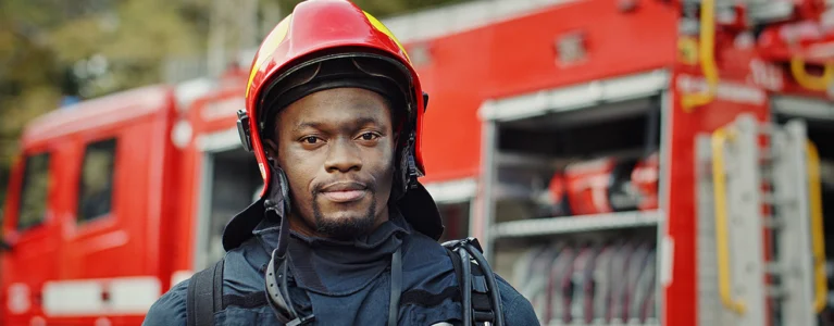 young black male firefighter stands in front of a firetruck