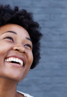 young black woman stands in front of a blue wall smiling joyfully