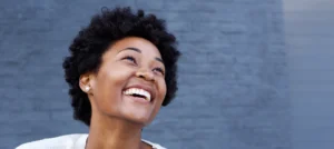 young black woman stands in front of a blue wall smiling joyfully