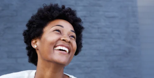 young black woman stands in front of a blue wall smiling joyfully