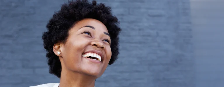 young black woman stands in front of a blue wall smiling joyfully