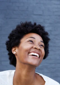 young black woman stands in front of a blue wall smiling joyfully