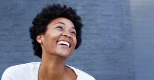 young black woman stands in front of a blue wall smiling joyfully