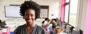 smiling teacher with students working at computers behind her